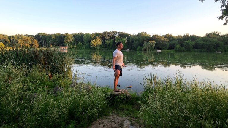 Dr. Chris Rivera practicing single-leg balance outdoors near a lake to support brain health & longevity.