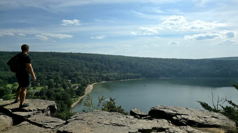 Hiker overlooking a lake and forest from a rocky overlook.